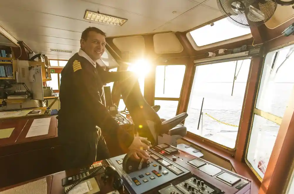 The captain at the controls on the bridge with the sun through the windows