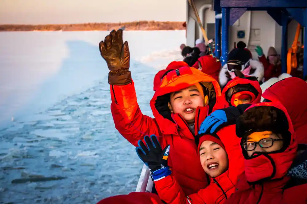 Children in survival suits with their arms up on the ice