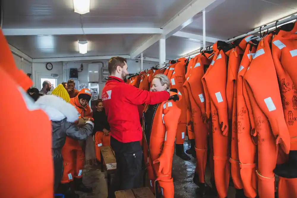 Crew fitting passengers into survival suits from racks in the changing room