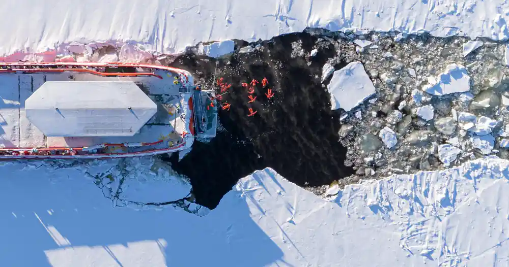Floating passengers gathered in the broken channel beside the hull, seen from above