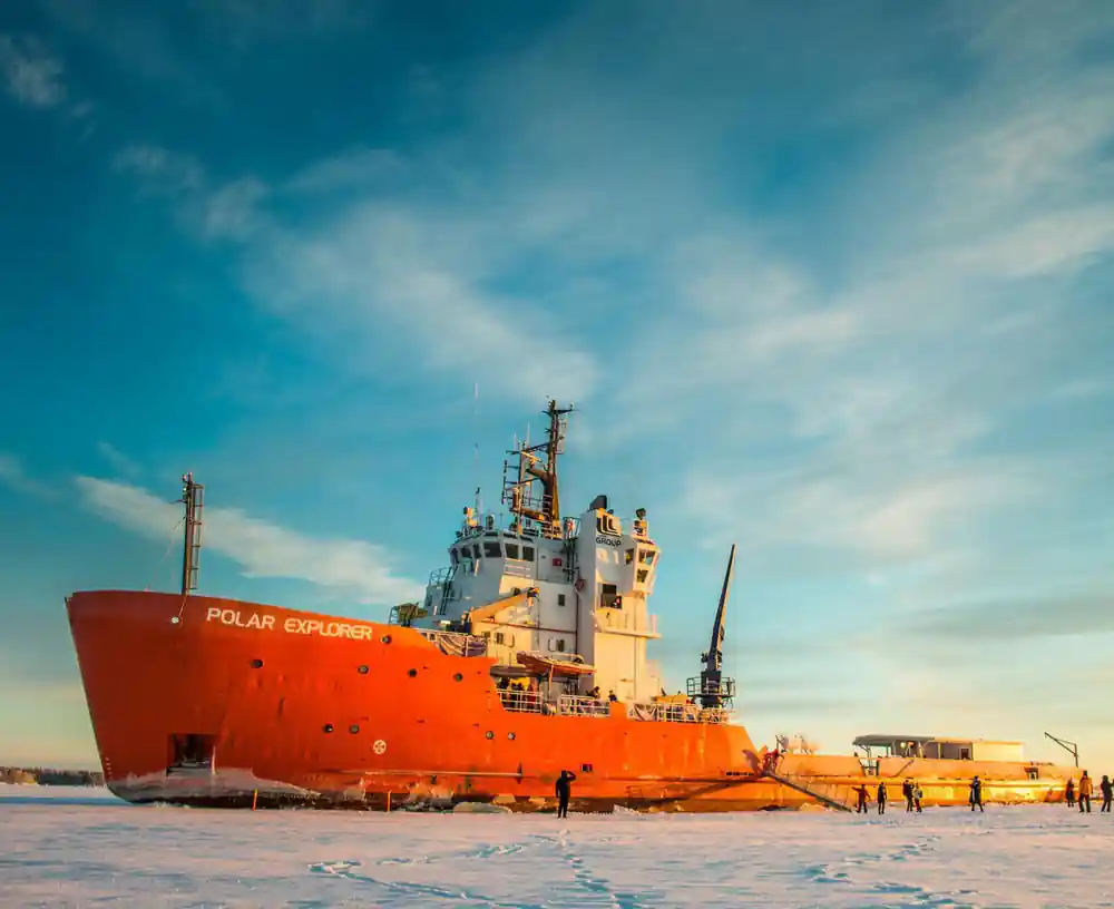 The icebreaker moored against the ice at low sun with people crossing to it