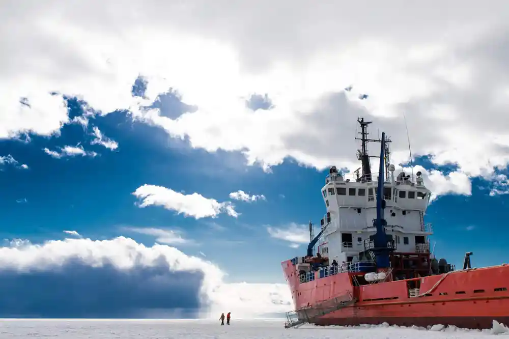 The icebreaker under a tall cloud with figures walking on the ice towards it