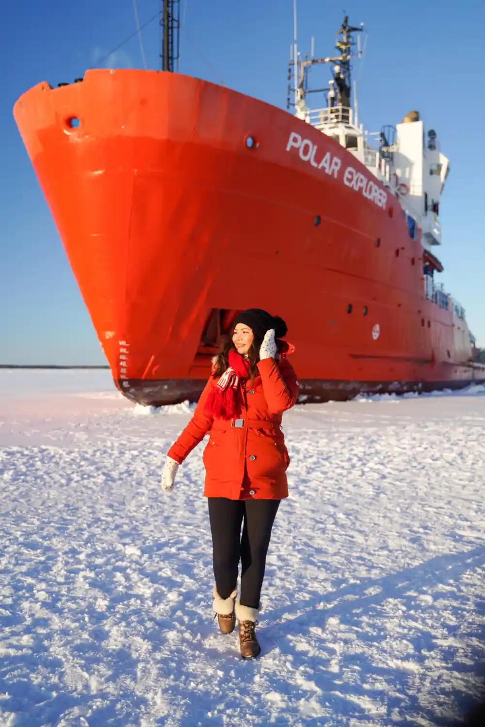 A passenger in a red coat standing on the ice below the ship name