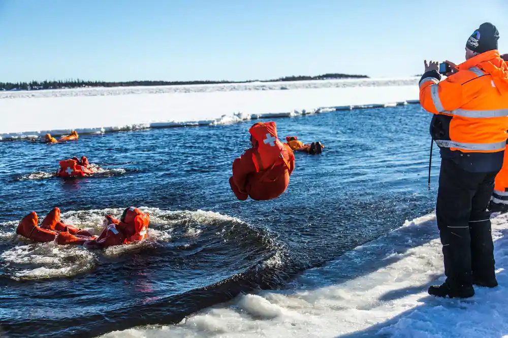 A passenger swimming in a survival suit at the edge of the ice