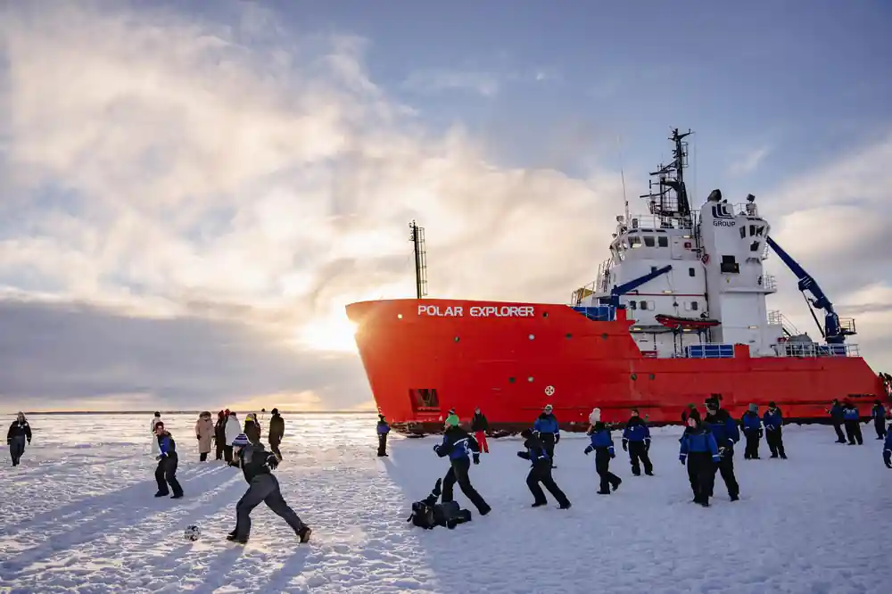 Passengers walking on the frozen sea beside the ship at sunset