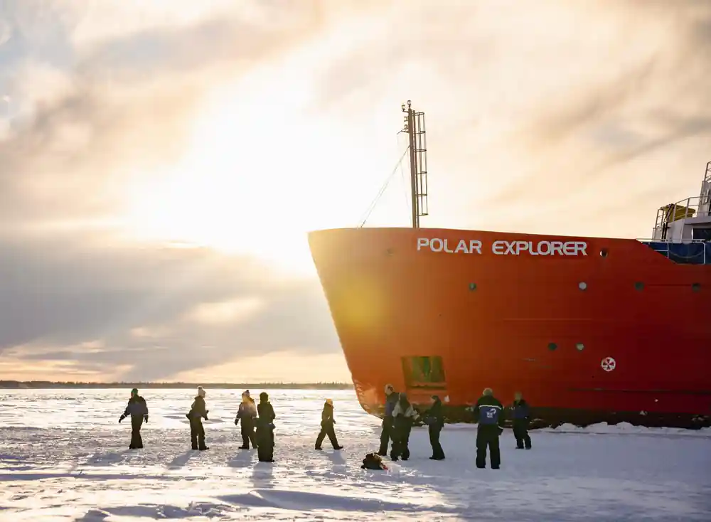 Passengers walking on the ice below the bow in low sun