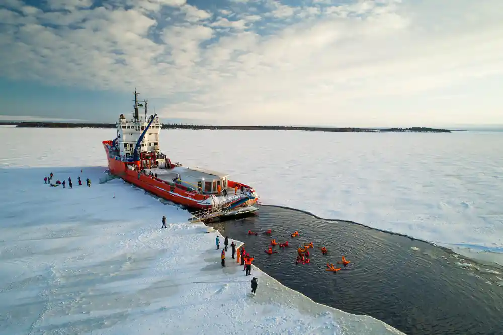 The ship in an open channel with people in orange suits in the water