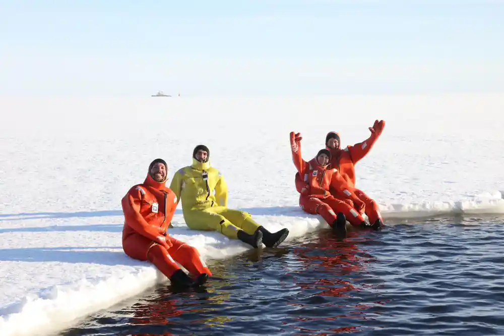 Three passengers in survival suits sitting on the ice edge before going in