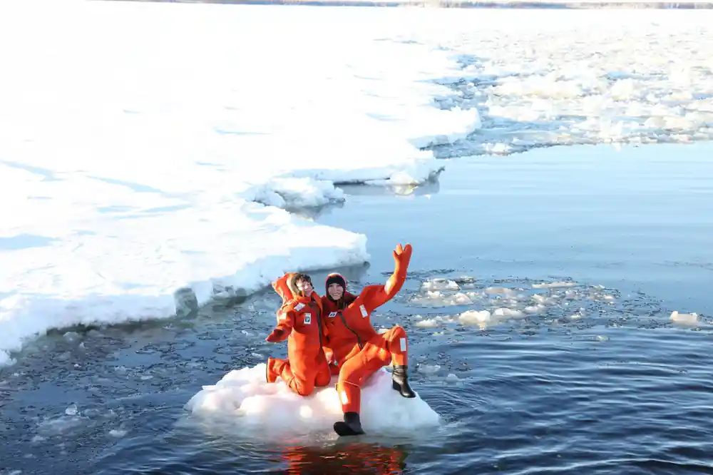 Two passengers in orange suits floating between slabs of broken ice