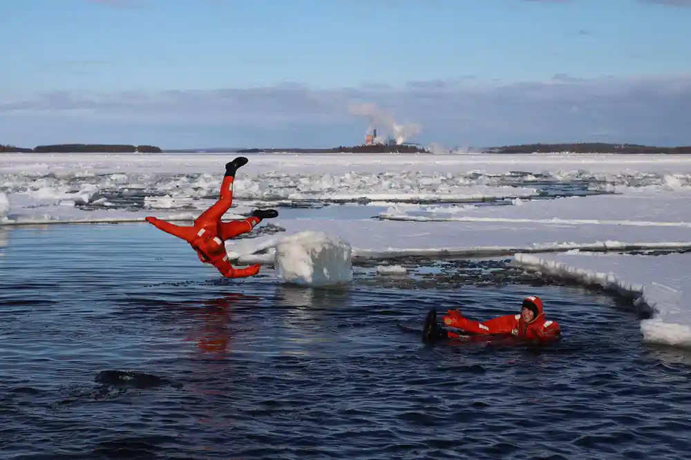 Two passengers in orange suits sliding into the water off the ice