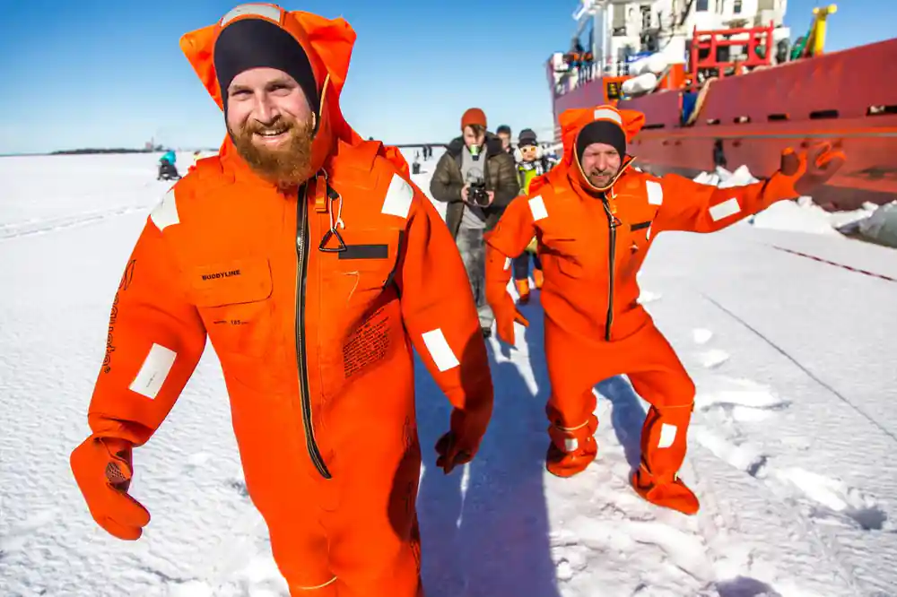 Two passengers in orange survival suits walking on the ice