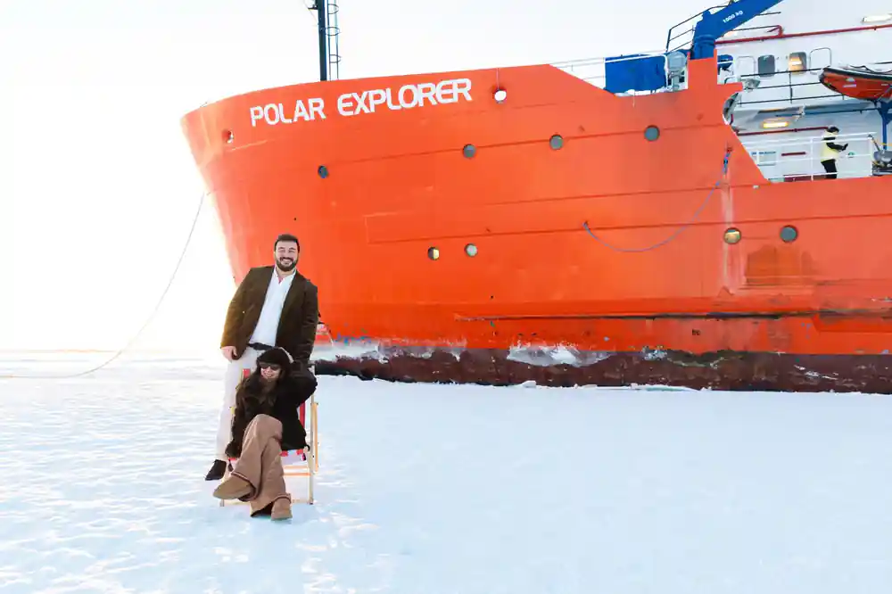 Two passengers posed against the red hull with the ship name above them