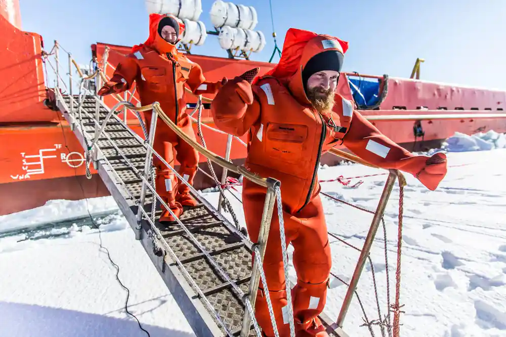 Two passengers in survival suits on the boarding stairs